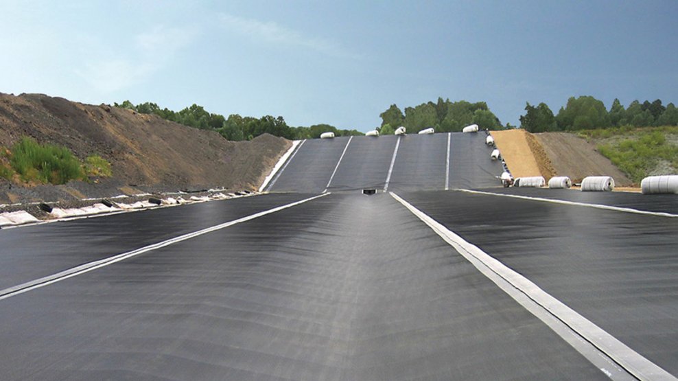 Extensive surface with welded membrane sheets and partially rolled materials inside an engineered excavation area.