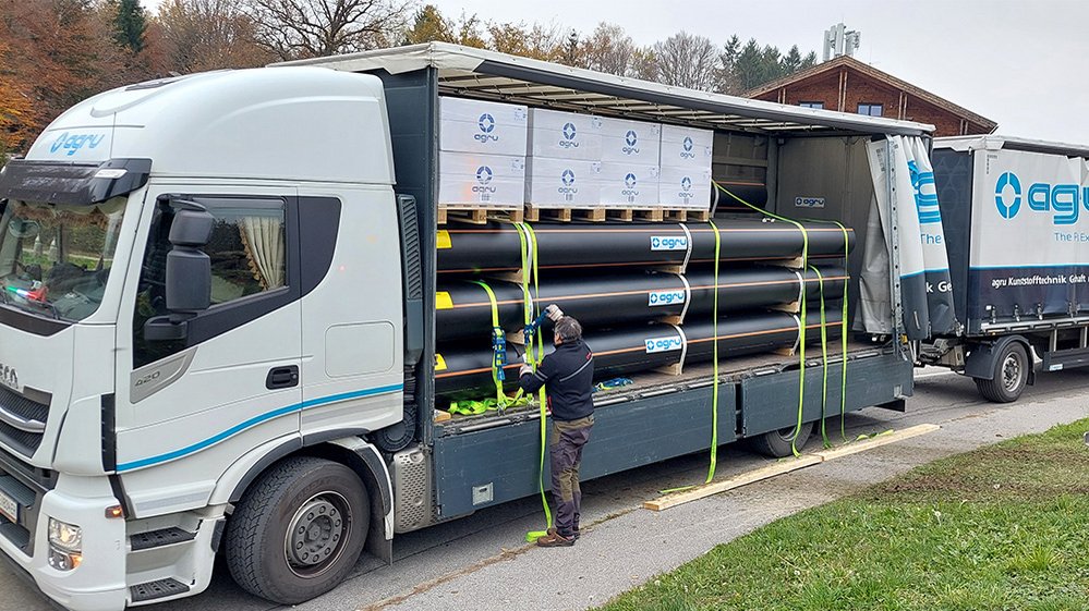 Loaded pipes and stacked boxes on pallets fixed with tension straps, person securing cargo on truck
