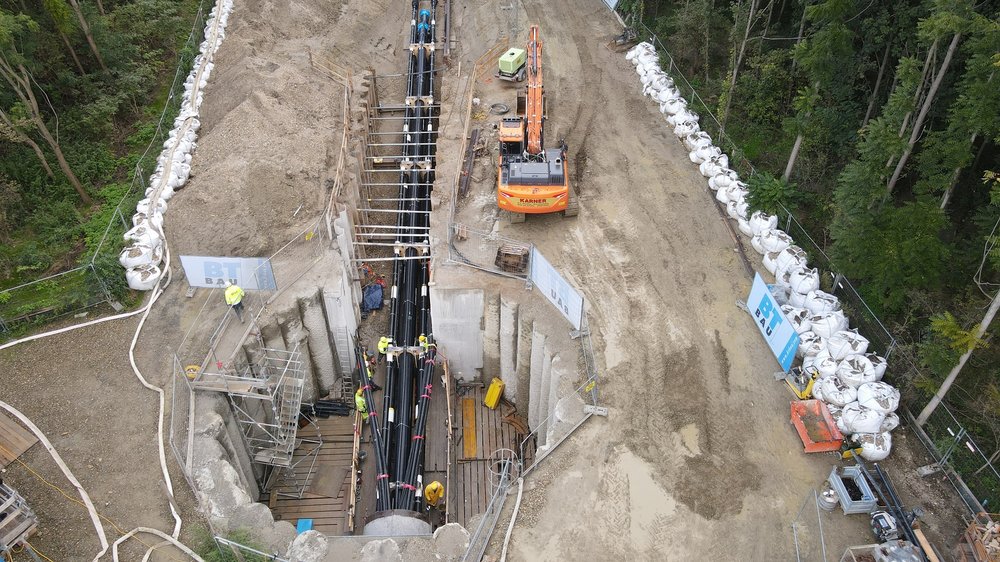 Construction site aerial view with pipeline installed in excavation, excavator and workers along open trench