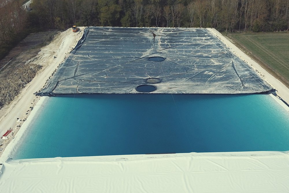 Folienausgekleidetes Reservoir mit Wasserfläche und schwimmender schwarzer Abdeckung in ländlicher Umgebung.