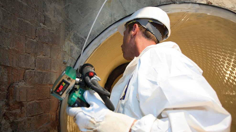Person in protective clothing welds a light-colored plastic liner inside a masonry pipe tunnel.