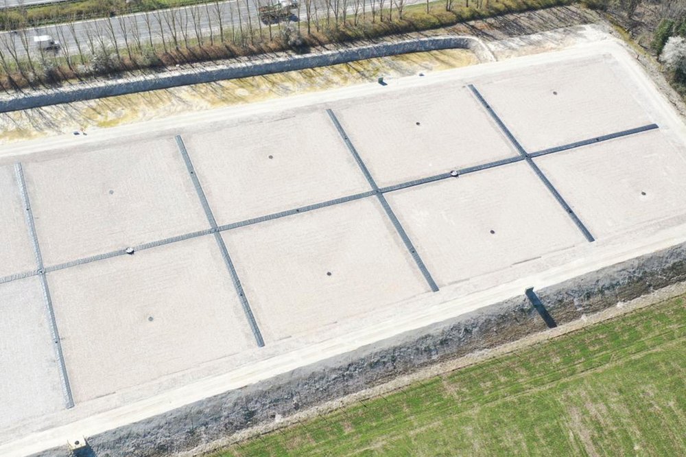 Rechteckiges Speicherbecken mit heller Auskleidung und rasterförmig angeordneten Entwässerungskanälen in ländlicher Umgebung.