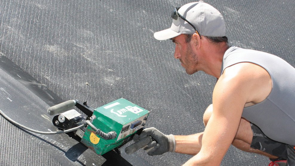 Close-up of welding work on a black membrane sheet with specialized equipment and protective gloves.