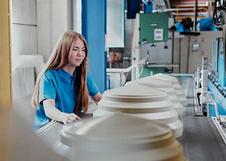 Lehrling überwacht Fertigungsprozess an Produktionslinie mit Kunststoffbauteilen und Fördertechnik