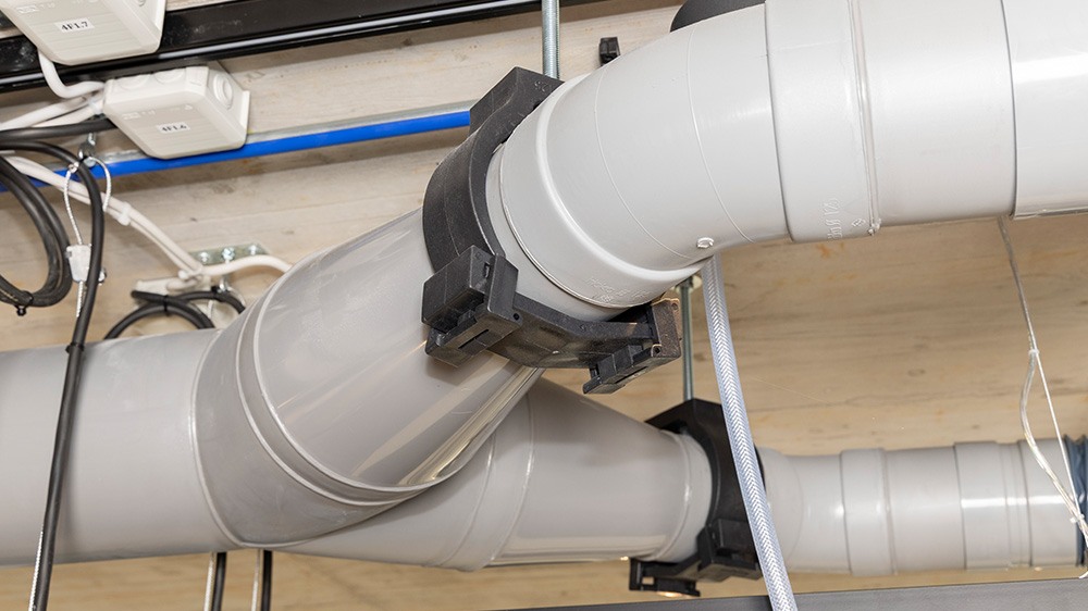 Curved duct section and main line of an industrial extraction system with sturdy mounting components.