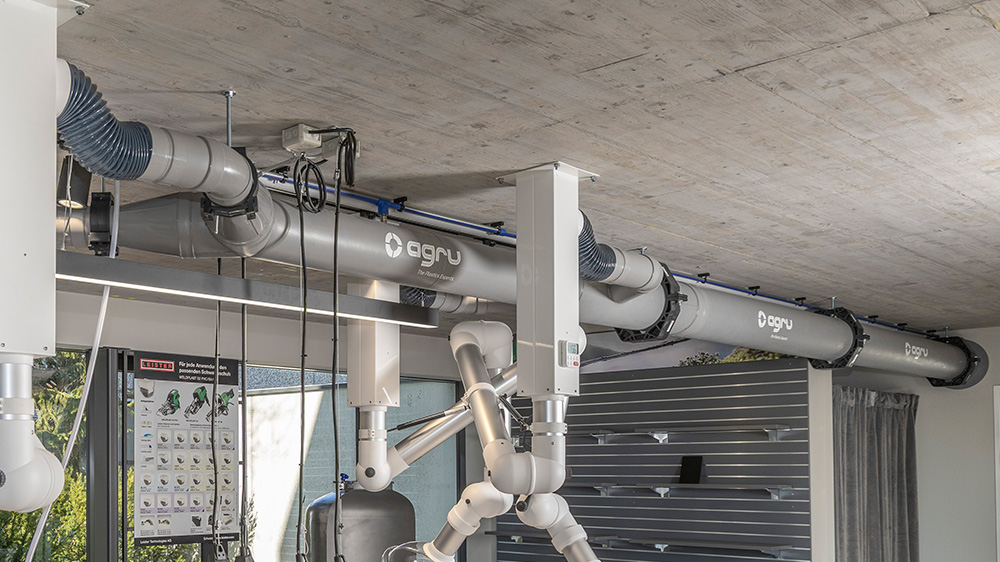 Ceiling-mounted extraction unit with plastic ductwork and adjustable extraction arms inside a workshop.