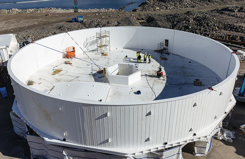 Large circular tank under construction, several people working inside, scaffolding and equipment on floor