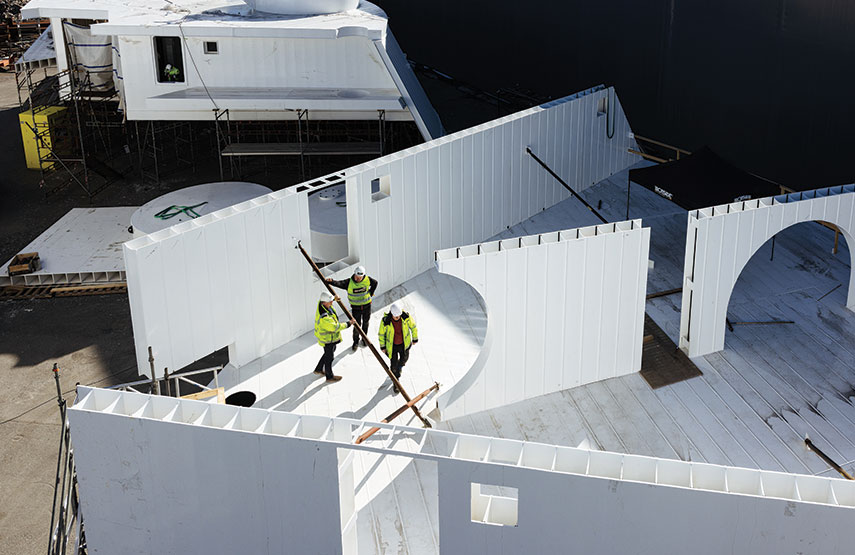Curved wall segments being assembled, three people working inside, large circular openings visible
